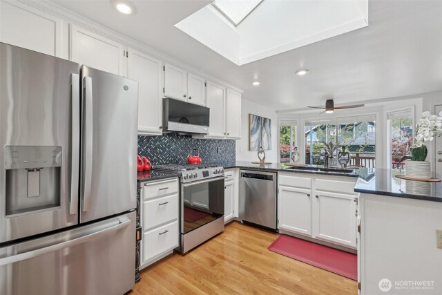 kitchen featuring tasteful backsplash, white cabinets, a sink, appliances with stainless steel finishes, and a skylight