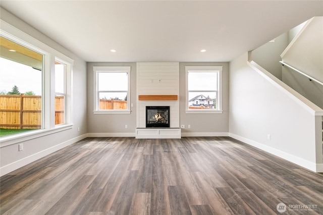 unfurnished living room with baseboards, a glass covered fireplace, wood finished floors, and a healthy amount of sunlight