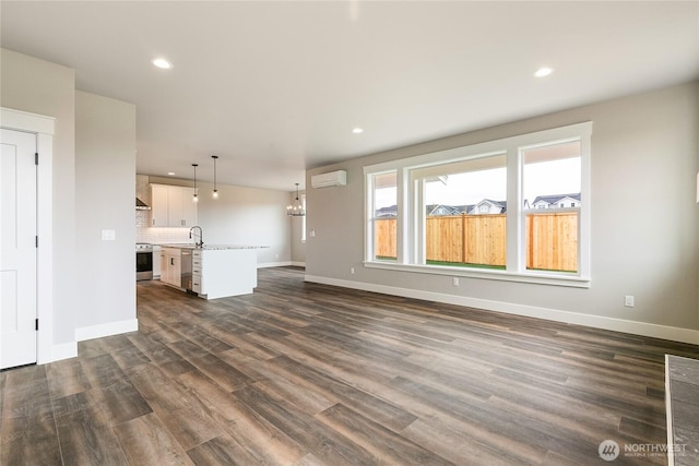 unfurnished living room with dark wood-style flooring, a wall mounted air conditioner, a sink, baseboards, and recessed lighting