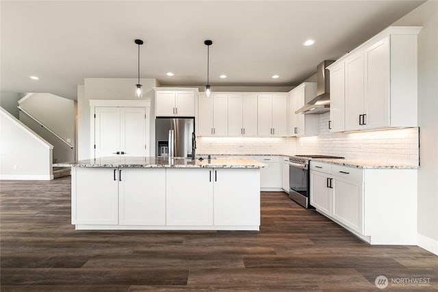 kitchen featuring wall chimney range hood, appliances with stainless steel finishes, white cabinets, recessed lighting, and an island with sink