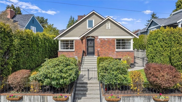 bungalow with brick siding, a chimney, a gate, and a fenced front yard