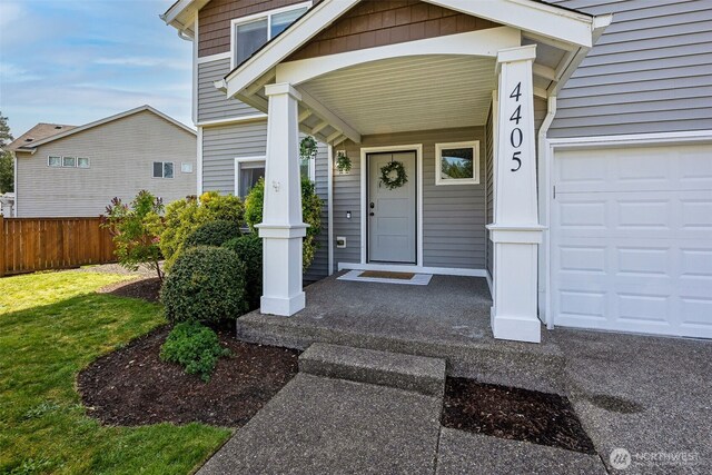 property entrance featuring fence, covered porch, an attached garage, and a yard