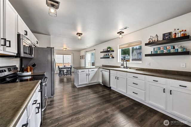 kitchen featuring open shelves, dark countertops, a sink, stainless steel appliances, and visible vents