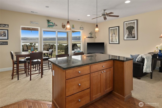 23154 Sunserra Loop NW Unit B15, Quincy, WA 98848 - kitchen featuring dark stone counters, a ceiling fan, brown cabinets, open floor plan, and carpet floors