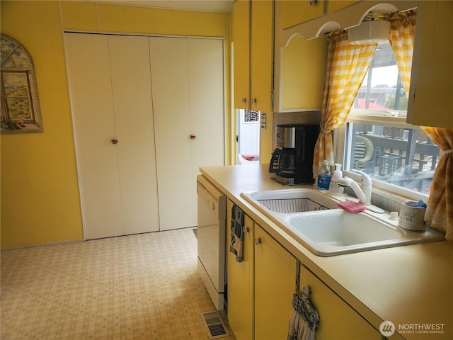 kitchen with light floors, light countertops, dishwasher, and a sink