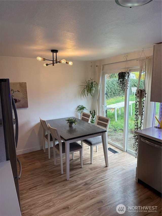 dining room with a textured ceiling, light wood-type flooring, baseboards, an inviting chandelier, and visible vents