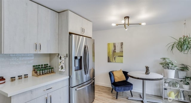 kitchen featuring stainless steel fridge with ice dispenser, light countertops, baseboards, light wood-style flooring, and tasteful backsplash