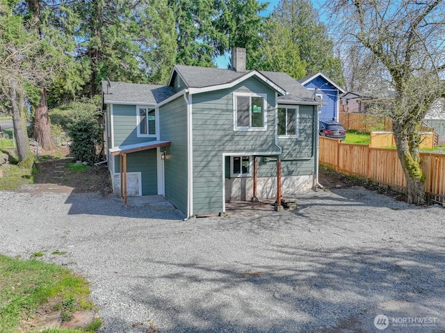 exterior space featuring roof with shingles, driveway, fence, and a chimney