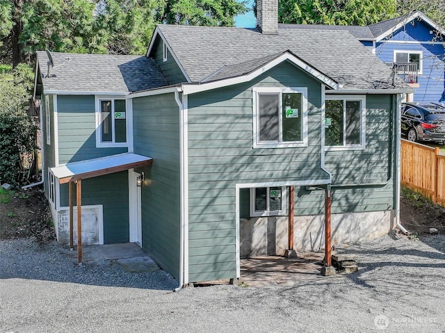 view of front of property with roof with shingles, a chimney, and fence