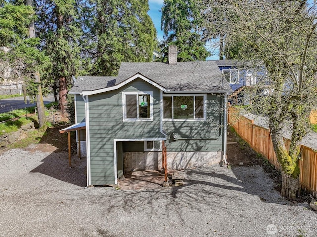 view of front of home featuring a shingled roof, fence, and a chimney