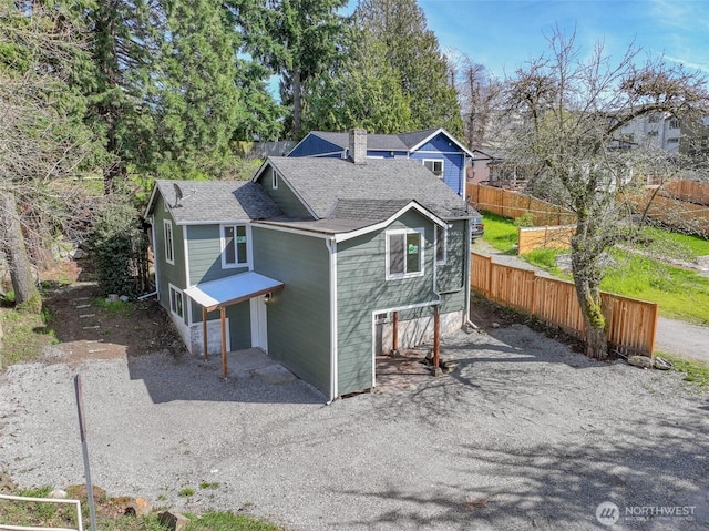 back of house with roof with shingles, fence, a chimney, a garage, and driveway