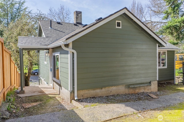 view of home's exterior featuring a chimney, fence, and a shingled roof