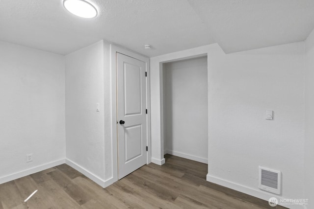 empty room featuring a textured ceiling, wood finished floors, baseboards, and visible vents