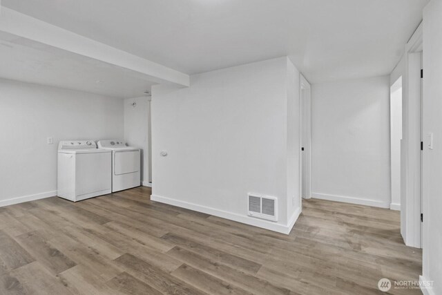 finished below grade area featuring visible vents, baseboards, washing machine and dryer, and wood finished floors