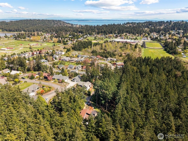 aerial view of property and surrounding area featuring a forest, a nearby body of water, and nearby suburban area