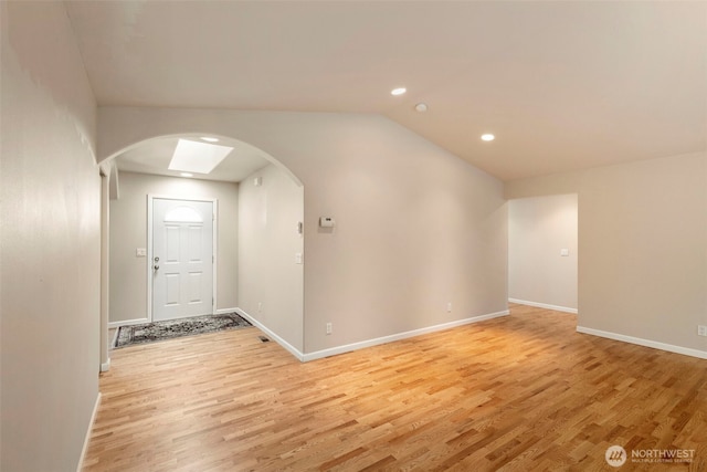 entryway featuring arched walkways, light wood finished floors, recessed lighting, baseboards, and lofted ceiling