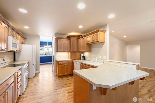kitchen featuring white appliances, a sink, a peninsula, a breakfast bar, and baseboards