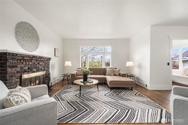 living area featuring a brick fireplace, baseboards, and wood finished floors