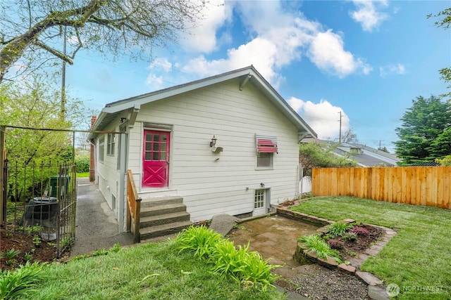 rear view of property with entry steps, a fenced backyard, and a yard