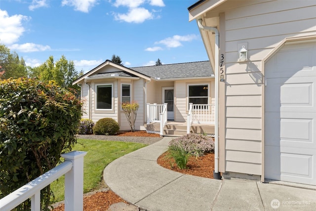doorway to property featuring a garage and roof with shingles