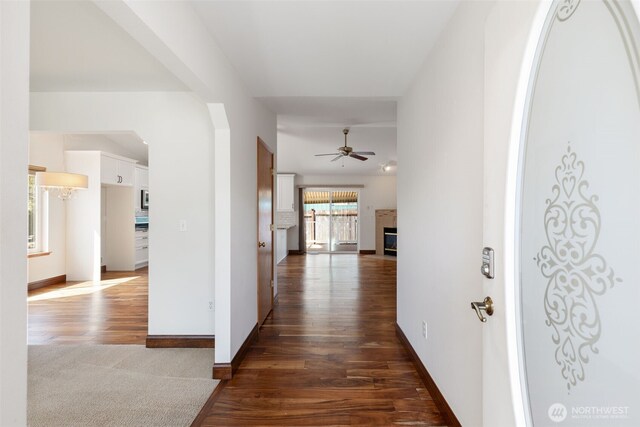 hall with dark wood-style flooring, arched walkways, and baseboards