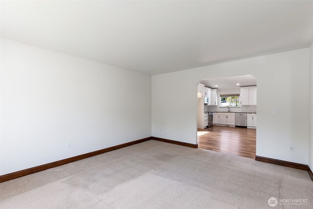 unfurnished living room with a sink, baseboards, arched walkways, recessed lighting, and light carpet