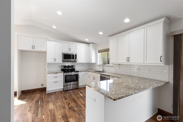 kitchen with a sink, a peninsula, light stone counters, white cabinetry, and appliances with stainless steel finishes