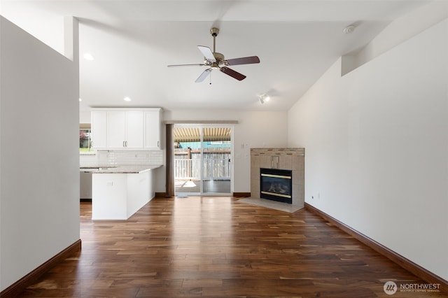 unfurnished living room featuring dark wood-style floors, ceiling fan, a tiled fireplace, and vaulted ceiling