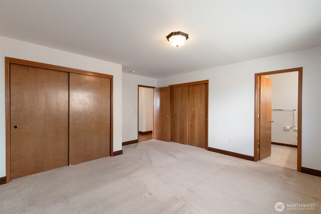 unfurnished bedroom with ensuite bath, light carpet, multiple closets, and baseboards