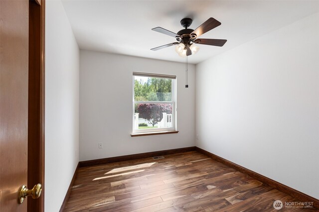 empty room featuring a ceiling fan, visible vents, baseboards, and dark wood finished floors