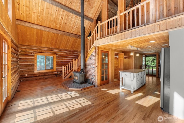 unfurnished living room with light wood-style flooring, a wood stove, beam ceiling, high vaulted ceiling, and wooden ceiling