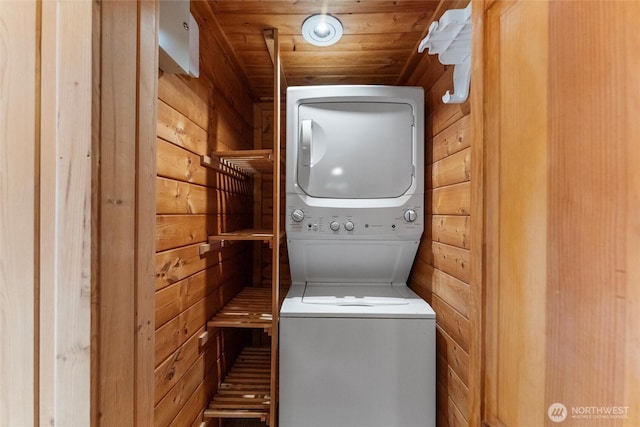 laundry room featuring stacked washing maching and dryer, wooden walls, wood ceiling, and laundry area