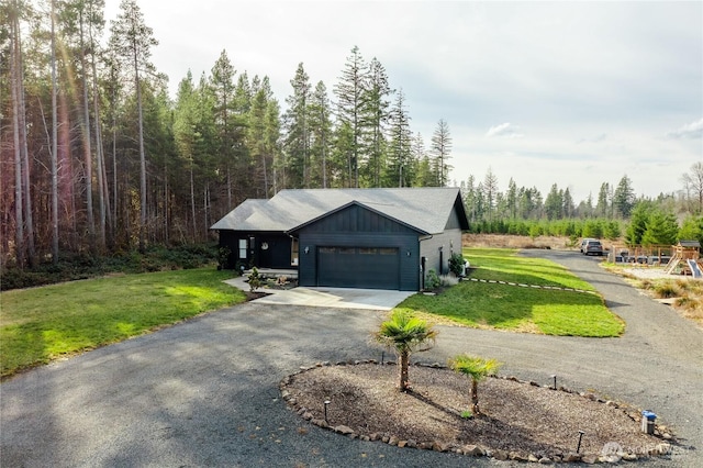 view of property exterior featuring board and batten siding, an attached garage, aphalt driveway, a forest view, and a lawn