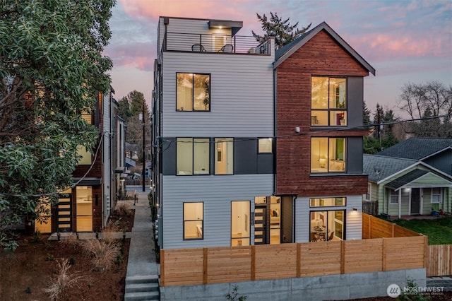 contemporary house featuring a balcony, a fenced front yard, and stairs