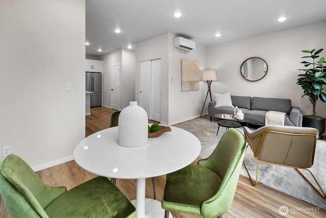 dining space featuring a wall unit AC, light wood finished floors, baseboards, and recessed lighting