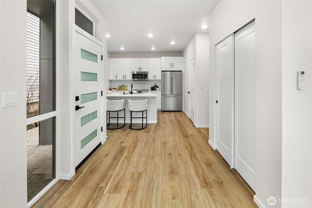 kitchen with white cabinets, light countertops, stainless steel appliances, backsplash, and a breakfast bar area