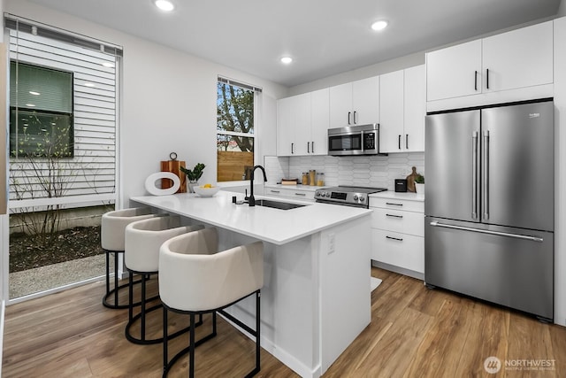kitchen featuring appliances with stainless steel finishes, white cabinetry, decorative backsplash, a sink, and wood finished floors
