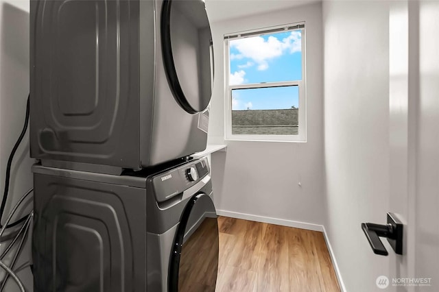 clothes washing area featuring baseboards, stacked washer / drying machine, laundry area, and wood finished floors