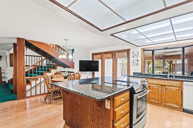 kitchen featuring light wood finished floors, a sink, stainless steel electric range oven, a notable chandelier, and white dishwasher