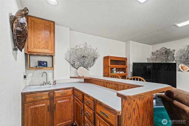 kitchen with a peninsula, light countertops, brown cabinetry, and a sink