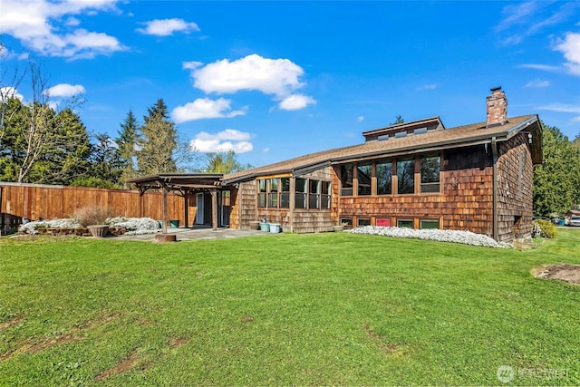 back of property featuring a lawn, a patio, a chimney, and fence