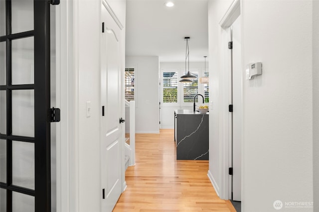 hall featuring recessed lighting, light wood finished floors, baseboards, and a sink