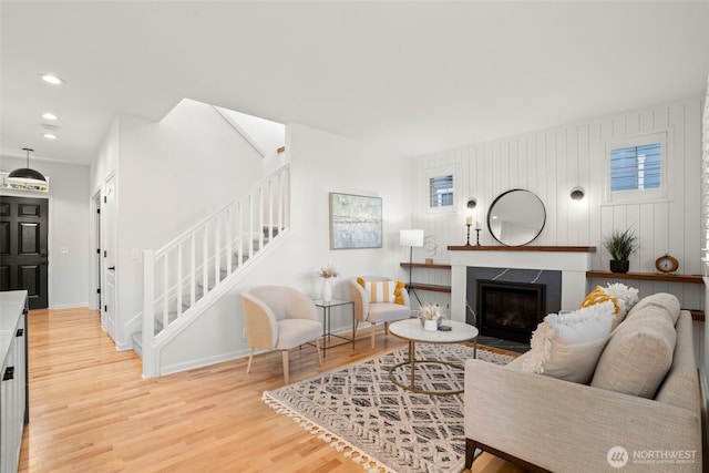 living room featuring baseboards, light wood-type flooring, recessed lighting, a fireplace with flush hearth, and stairs