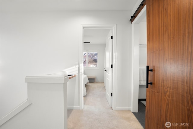 corridor featuring light colored carpet, baseboards, and a barn door