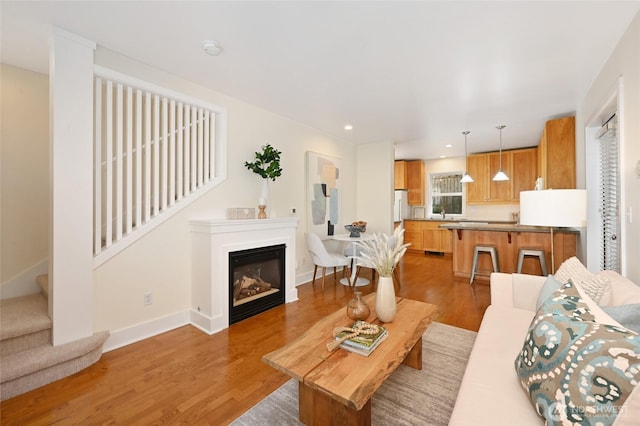 living room with light wood-style floors, a glass covered fireplace, recessed lighting, baseboards, and stairway