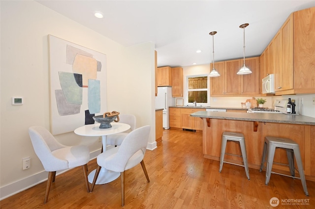 kitchen with a peninsula, white appliances, light wood-style floors, a kitchen bar, and a sink