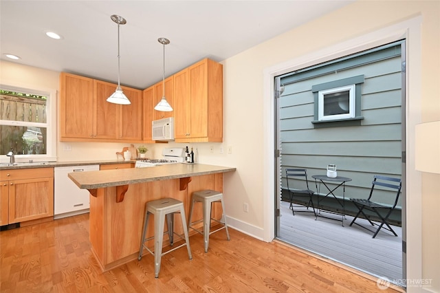 kitchen with a sink, light wood finished floors, white appliances, a kitchen breakfast bar, and pendant lighting