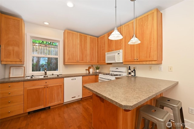 kitchen with a kitchen bar, dark wood finished floors, a sink, a peninsula, and white appliances