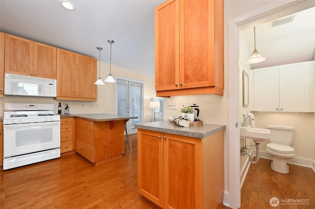 kitchen featuring a peninsula, white appliances, wood finished floors, and decorative light fixtures