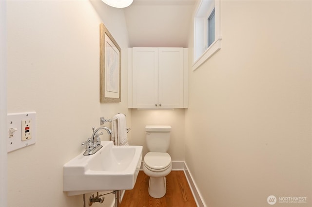 half bath featuring baseboards, a sink, wood finished floors, and toilet